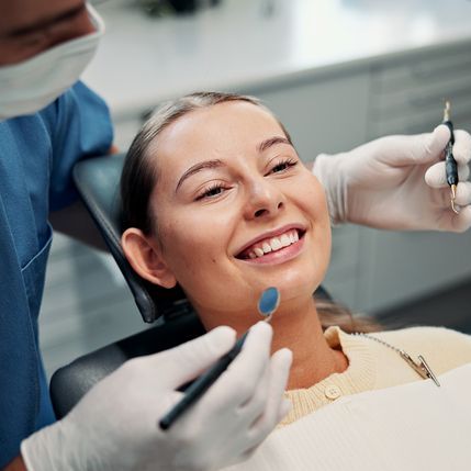 Patient smiling in a dental chair while a masked clinician examines their teeth