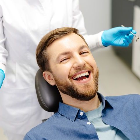 Patient smiling in a dental chair while a clinician holds a dental mirror